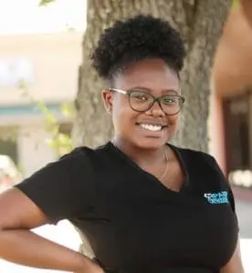A person wearing glasses and a black shirt, standing outdoors with trees and buildings in the background, exudes confidence as a stylish braces porter.