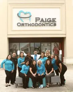 The dedicated team of orthodontic staff from Paige Orthodontics posed proudly in front of the office building, set against the backdrop of a large sign displaying their practice name and logo. They're ready to provide top-notch braces for Porter, TX residents.