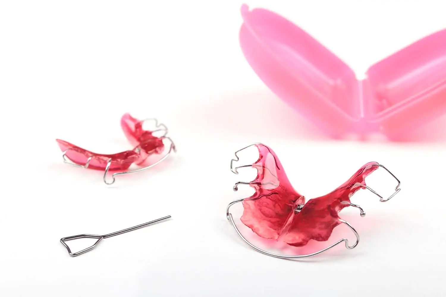 two pink dental retainers with metal wires are displayed alongside a small metal tool at Paige Orthodontics in Kingwood, TX