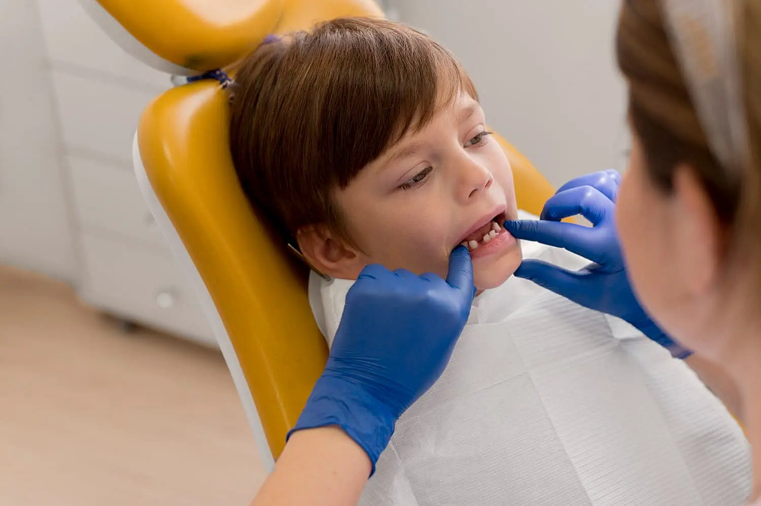 A dentist in blue gloves examines problem a child's teeth in Kingwood TX at Paige Orthodontics in Kingwood, TX