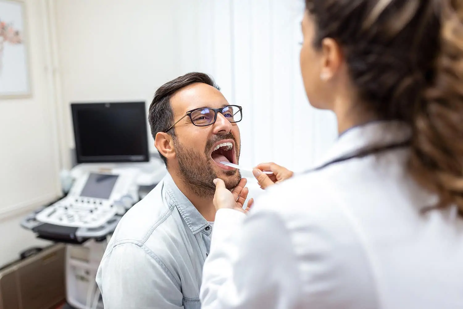 a doctor uses a tongue depressor to examine a man's throat at Paige Orthodontics medical office in a Kingwood TX
