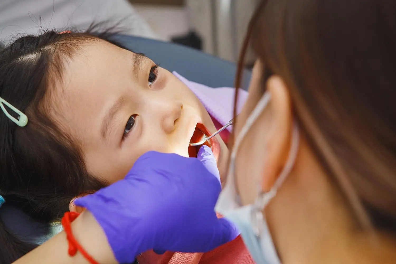 Young girl in a dental chair having her tongue thrust examined by a dentist using a dental mirror and probe at Paige Orthodontics in kingwood, TX