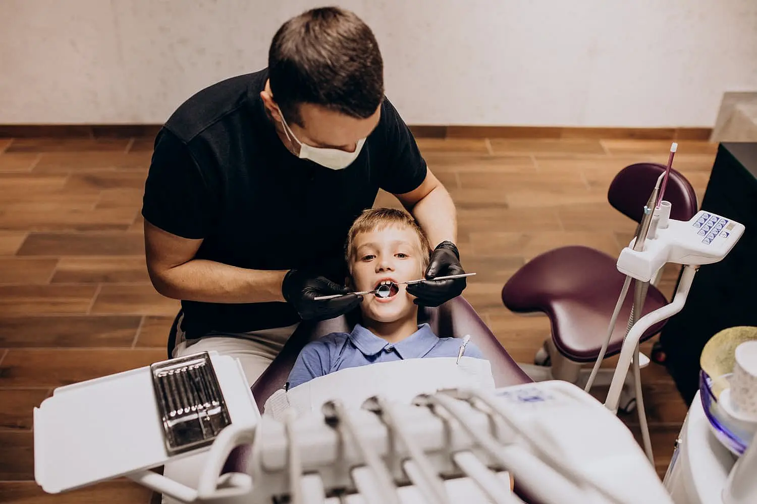 a dentist wearing gloves and a mask examines a boy's teeth in the dental chair at Paige Orthodontics in Kingwood, TX