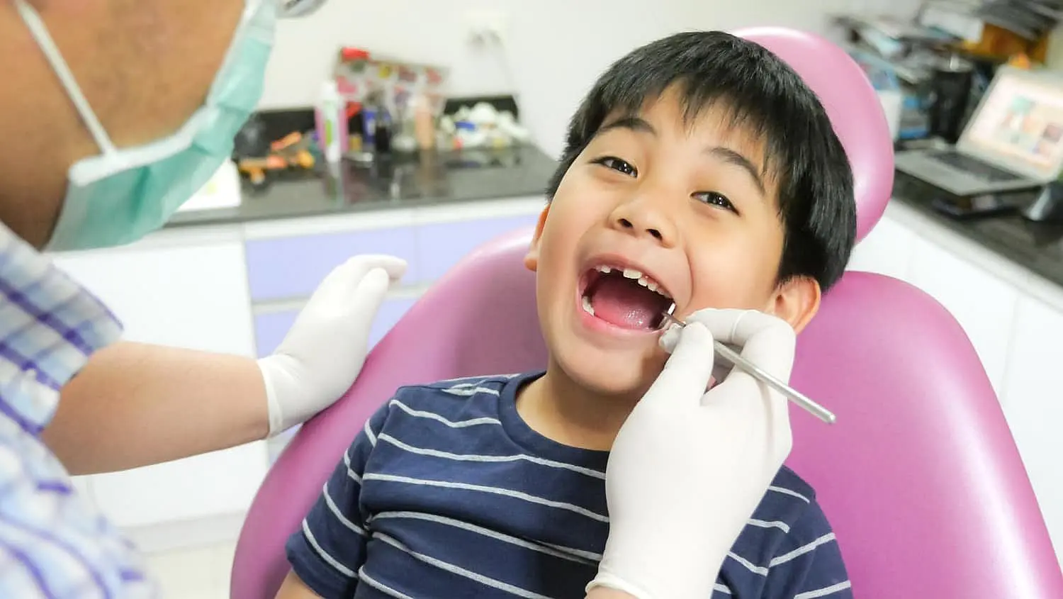 A child is examined by a dentist while sitting in a dental chair with an open mouth at Paige Orthodontics in Kingwood, TX