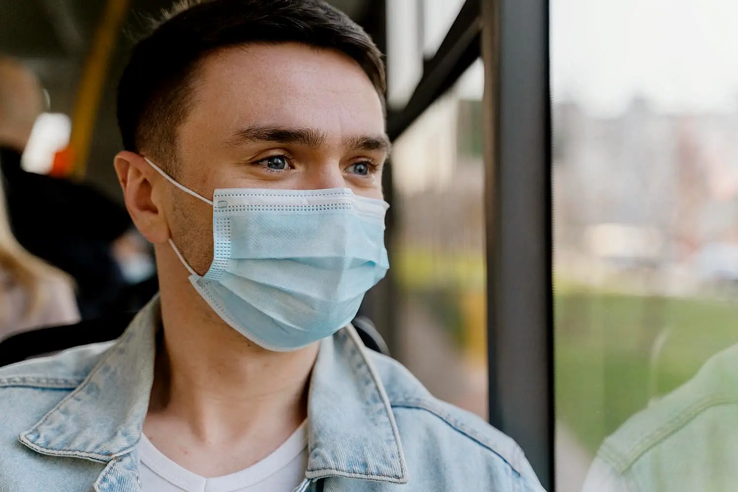 On a bus in Kingwood TX, a man in a denim jacket wears a face mask and gazes out the window, careful not to mouth breathe.
