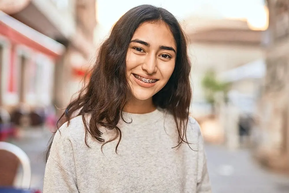 A young woman in Kingwood TX confidently smiles outdoors, showcasing her metal braces.