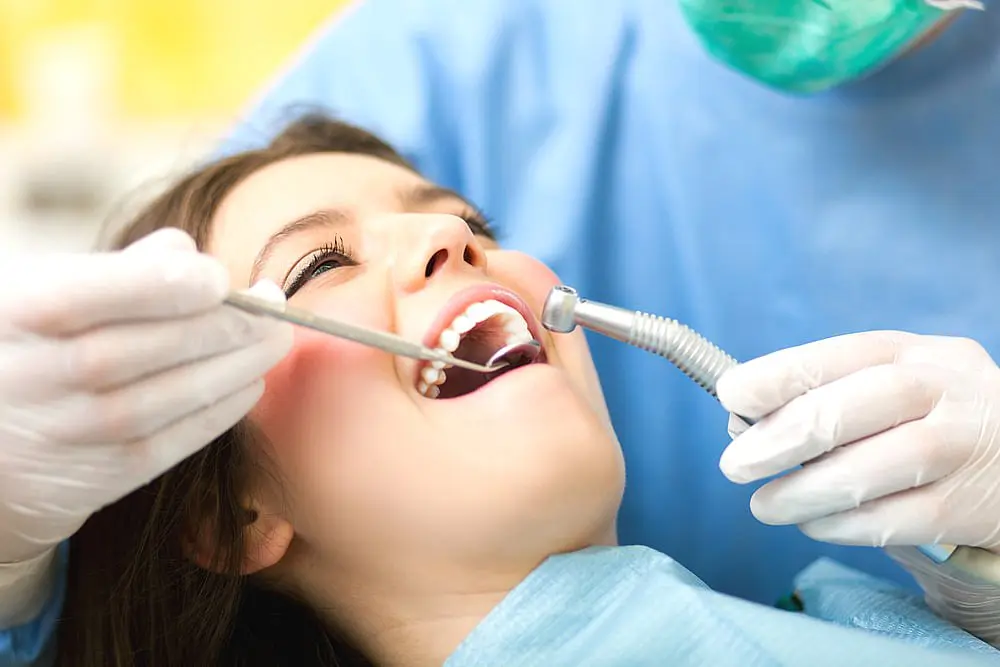 In Kingwood TX, a dentist, wearing gloves and using precise tools, examines a patient's teeth for signs of an underbite while the patient lies back with their mouth open.