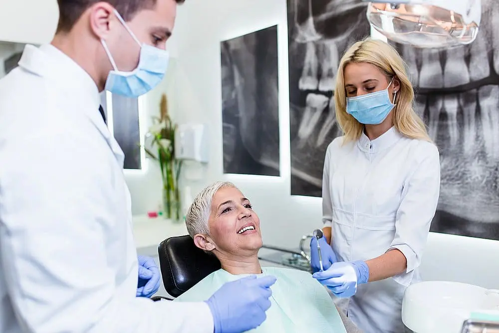 A woman is sitting in a dental chair, receiving treatment from two dental professionals at Paige Orthodontics in Kingwood, TX