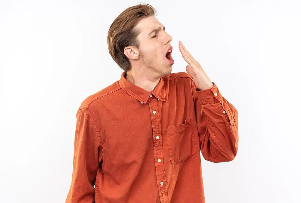 Against a white background, someone in an orange shirt yawns, subtly showing mouth breathing. They cover their mouth in this Kingwood TX scene.
