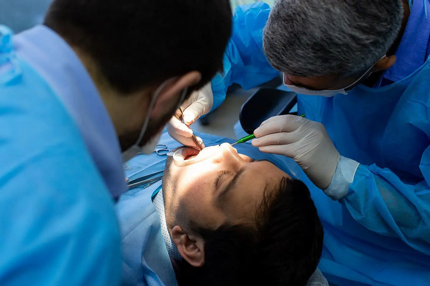 Two dentists in blue scrubs perform a tongue on a patient lying on an examination chair at Paige Orthodontics in kingwood, TX