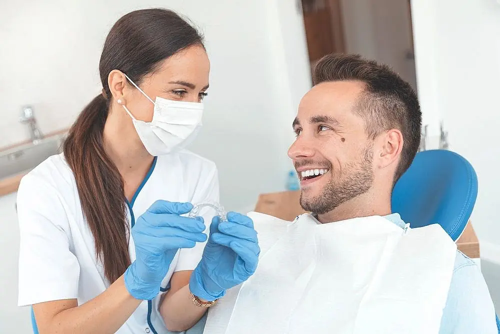 At Paige Orthodontics, an orthodontist in Kingwood, TX, showcases a clear aligner to a smiling patient, emphasizing how Invisalign insurance can make the perfect smile more attainable.