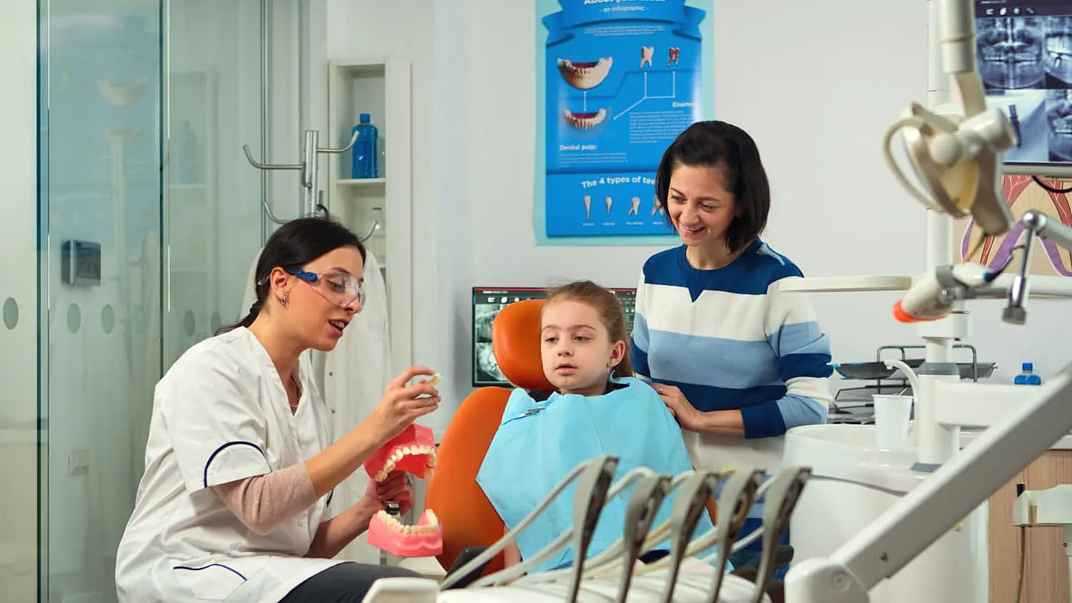 a dentist uses a model to demonstrate dental care to a young girl in the chair at Paige Orthodontics in Kingwood, TX