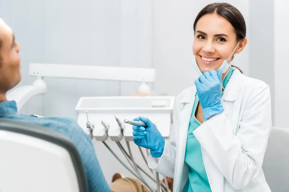 Dentist wearing gloves and a mask holds a dental tool, smiling at a seated patient at Paige Orthodontics in Kingwood, TX
