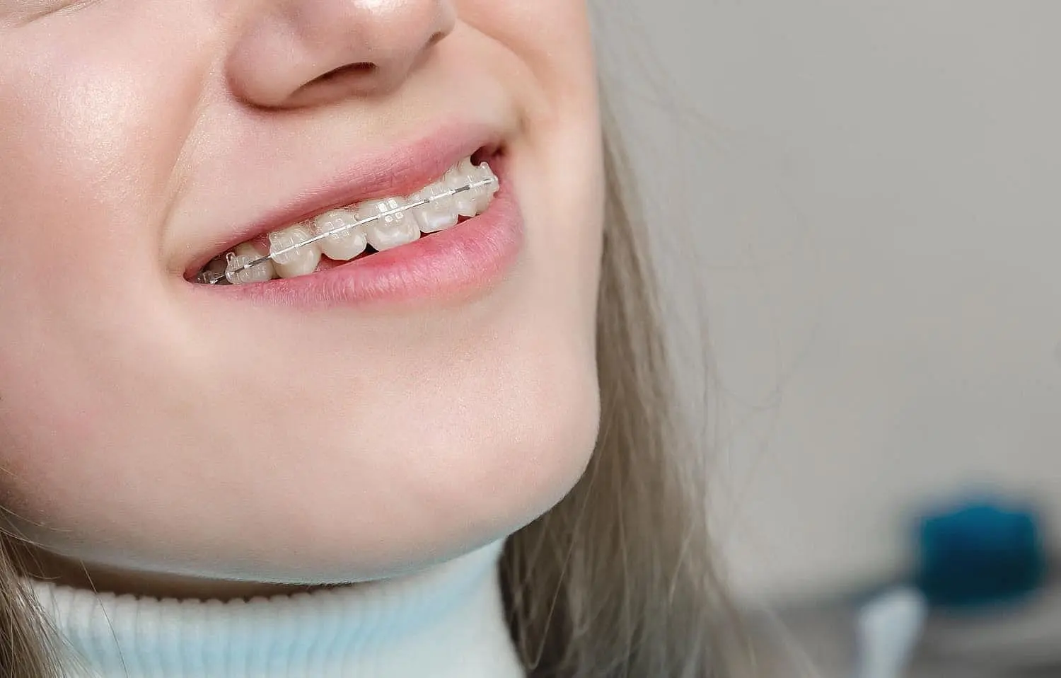 A woman wearing ceramic braces and a white high-neck top at Paige Orthodontics in Kingwood, TX