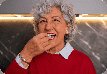 An elderly woman with curly hair, wearing a red sweater, enjoys sitting at Paige Orthodontics in Kingwood, TX