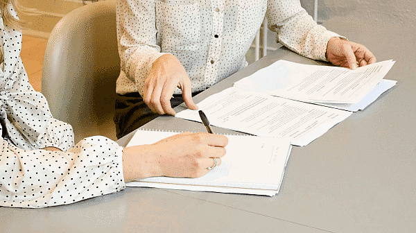 Two people sit at a table in Kingwood TX, reviewing documents insurance dental with one pointing at the papers using a pen at Paige Orthodontics in Kingwood, TX