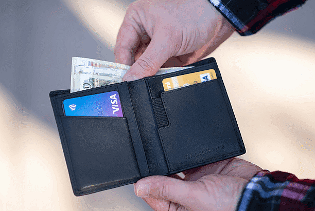 A person holding a black wallet with visible cash and two credit cards for Invisalign Payment plan at Paige Orthodontics in Kingwood, TX.