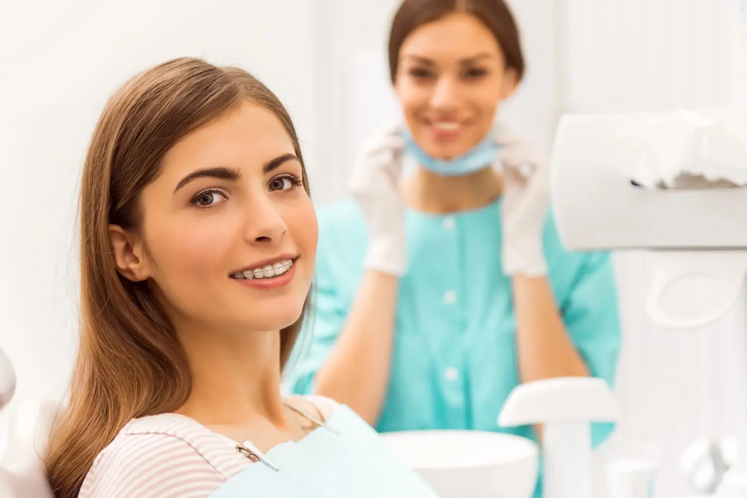 A woman with braces sits in a dental chair, smiling at the camera at Paige Orthodontics in Kingwood, TX