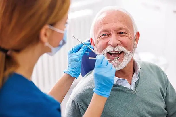 A dentist meticulously examines an older recommending jaw surgery while wearing gloves and holding dental tools At Paige Orthodontics in Kingwood, TX