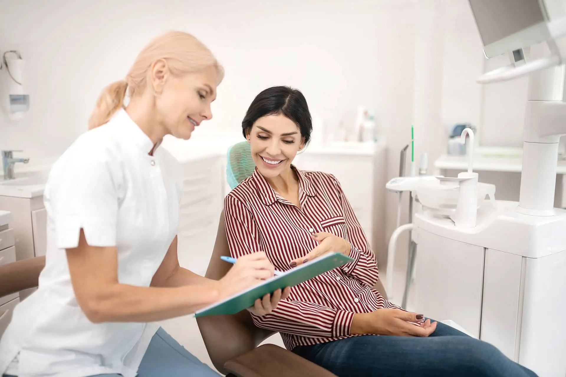 An orthodontist showing a clipboard explaining cheap Invisalign cost in Paige Orthodontics in Kingwood, TX to a patient seated in a dental chair, both smiling.