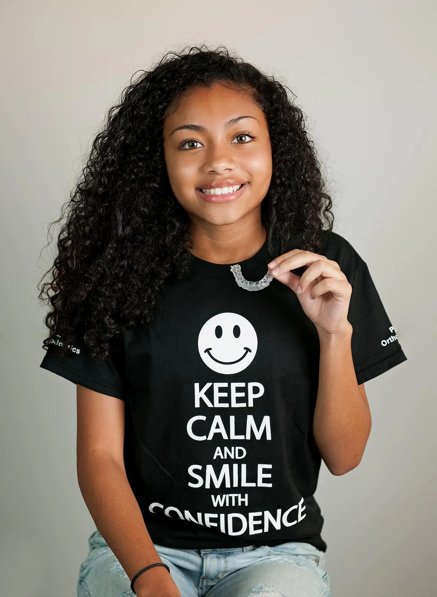 A smiling woman proudly displays their Invisalign clear dental aligner at Paige Orthodontics in Kingwood, TX