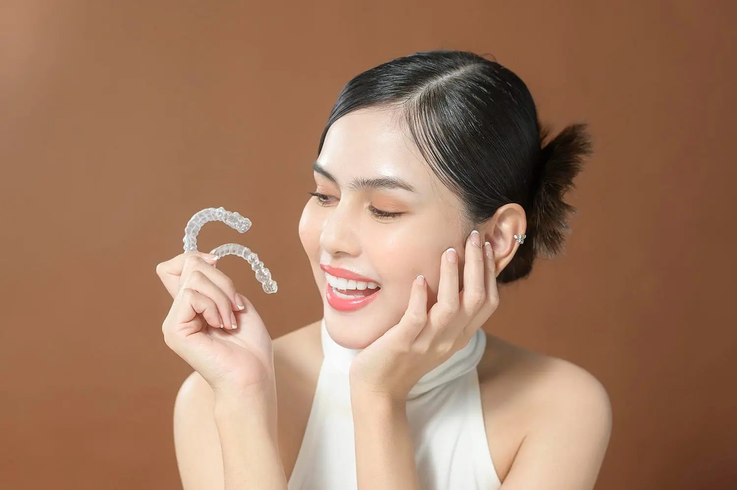 Smiling, a person holds dental aligners against a brown backdrop in Kingwood TX.