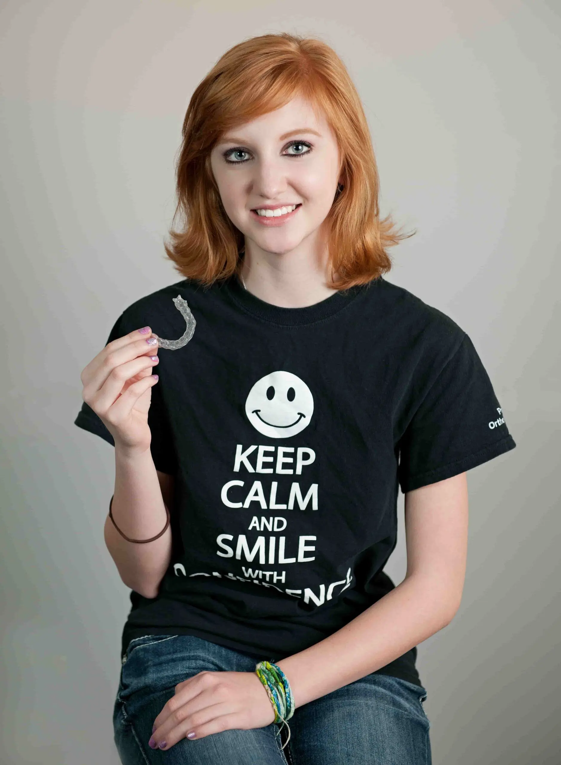 a young woman red-haired person in a black T-shirt holds a invisalign at Paige Orthodontics in Kingwood, TX
