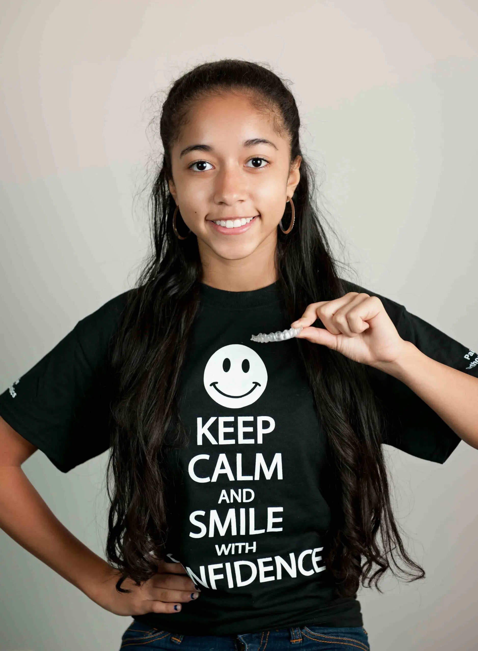 A young woman beams brightly, showcasing her invisalign clear aligner at Paige Orthodontics in Kingwood, TX