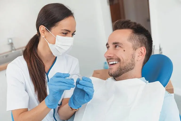 In Kingwood TX, a dentist in gloves and a mask presents an orthodontic aligner as one of the alternatives to braces in Kingwood, TX to a smiling patient.