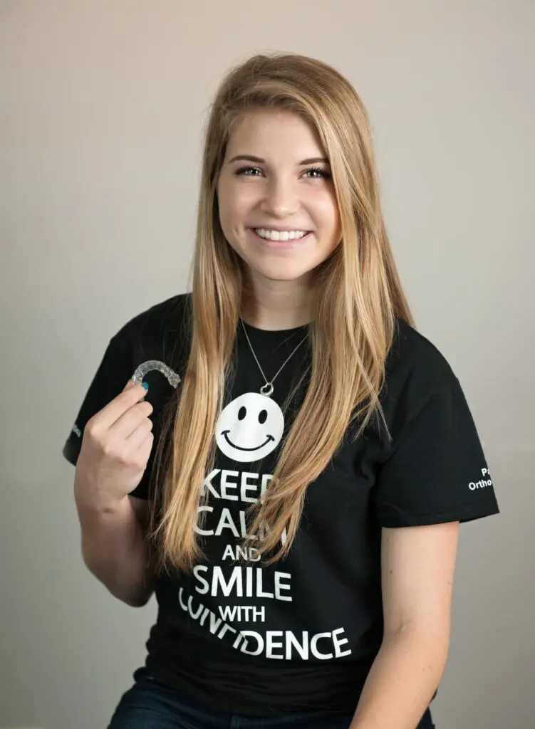 A smiling teenage boy with braces holds dental tools against a light blue background in Kingwood TX - How to Floss with Braces in Kingwood, TX A smiling teenage boy with braces holds dental tools against a light blue background in Kingwood TX - How to Floss with Braces in Kingwood, TX