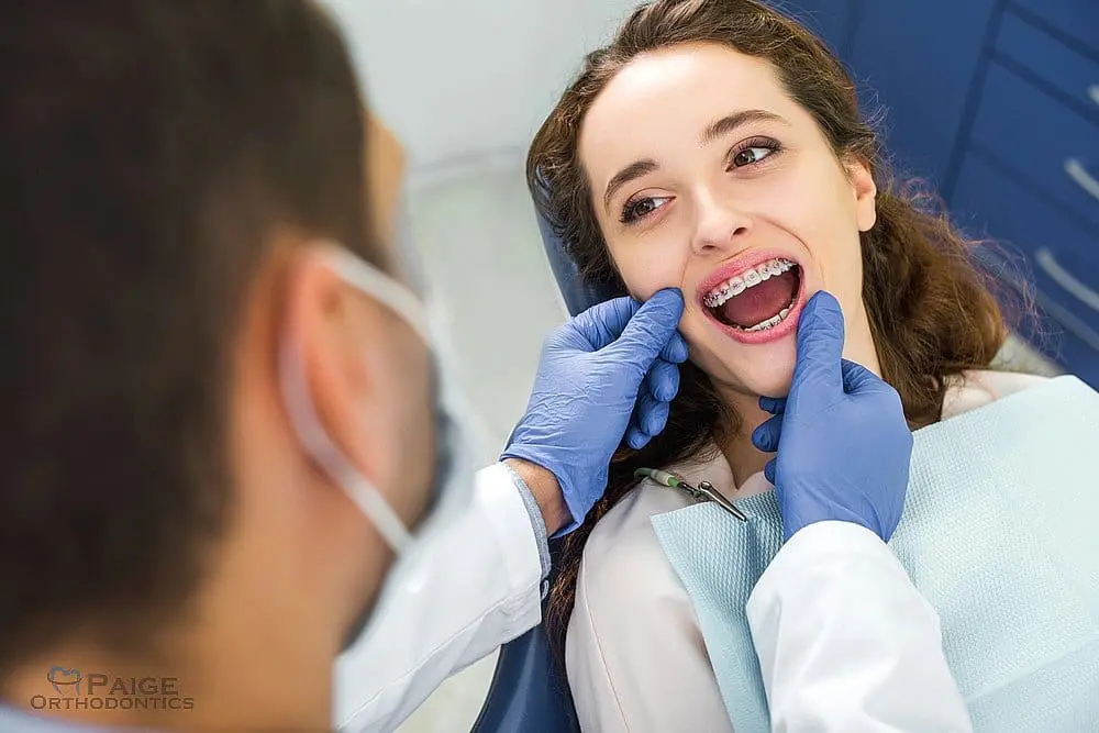 During an orthodontic appointment the patient is explained about how to fix overbite in Kingwood TX, a dentist wearing gloves examines a young woman with braces.