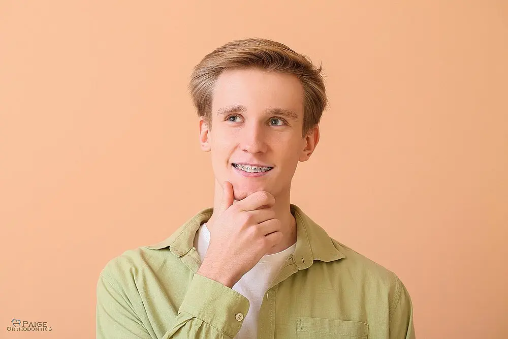 A smiling teenage boy with braces holds dental tools against a light blue background in Kingwood TX - How to Floss with Braces in Kingwood, TX