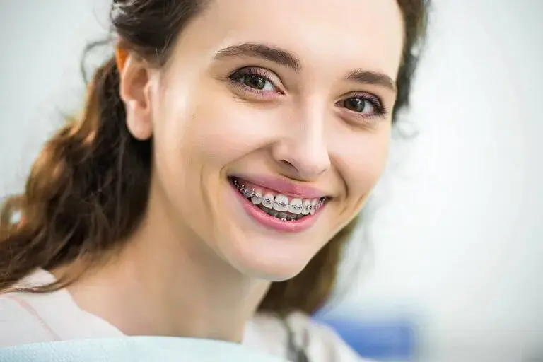 A young woman with long brown hair smiles, showing metal braces, in a Kingwood TX orthodontic office - Overbite vs Underbite in Kingwood, TX